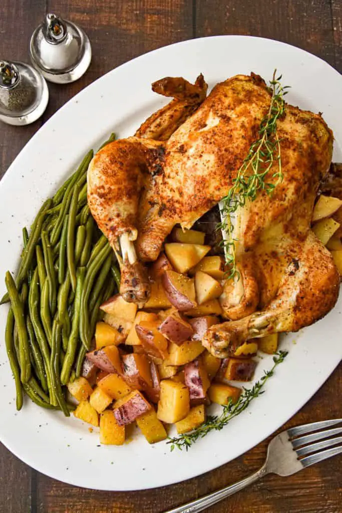 overhead shot of low fodmap instant pot whole chicken one pot meal with green beans and red potatoes on a white platter next to salt and pepper shakers on a brown wood background
