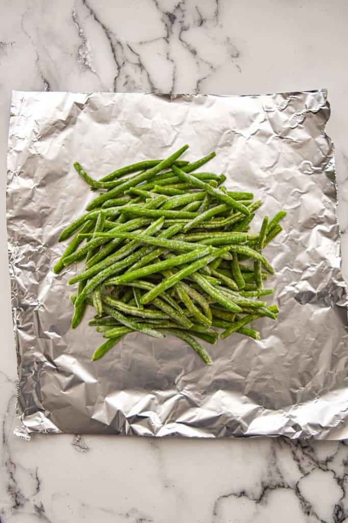 frozen green beans on tin foil on a white marble background