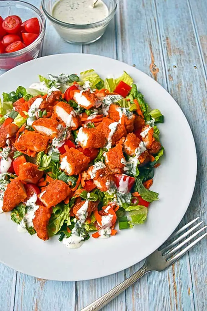low fodmap buffalo chicken salad dressed with low fodmap salad dressing on a plate next to bowls of ranch dressing and cherry tomatoes