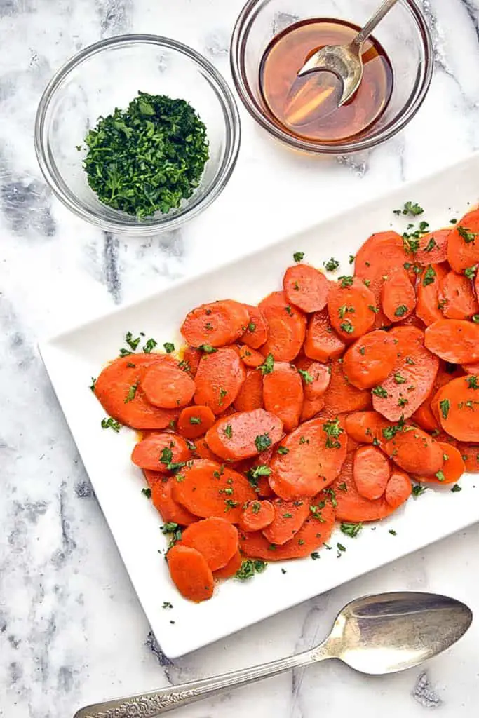 a plate of low fodmap instant pot glazed carrots next to bowls of maple syrup and chopped parsley