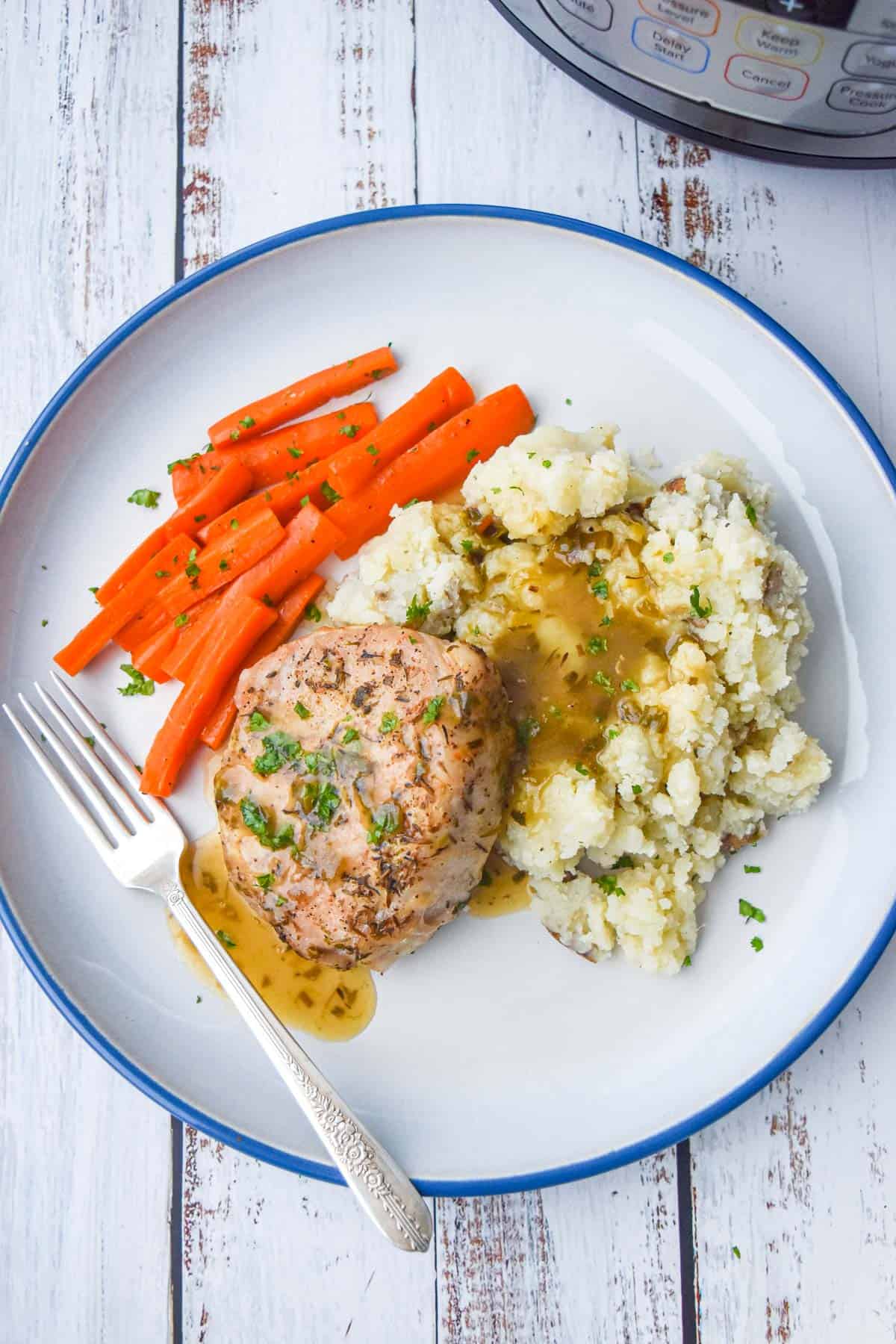 a cut pork chop laying on mashed potatoes and carrots and covered in gravy on a blue rimmed plate
