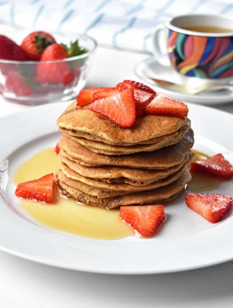 A plate of stacked tigernut flour pancakes topped with strawberries and maple syrup