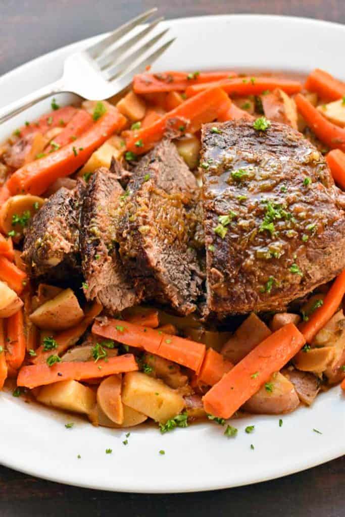 Sliced low fodmap beef pot roast, carrots, potatoes and mushrooms on a platter with a large serving fork.