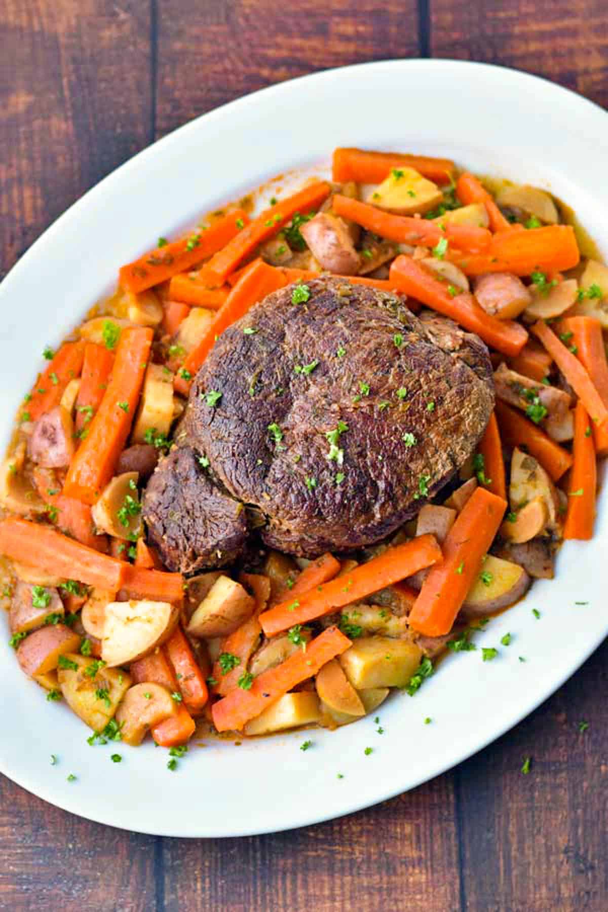 pot roast on a white platter surrounded by carrots and red potatoes