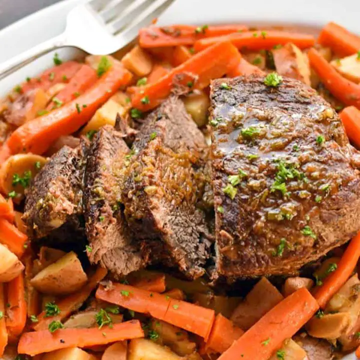 overhead shot of low fodmap pot roast sliced on a white platter with carrots and potatoes.