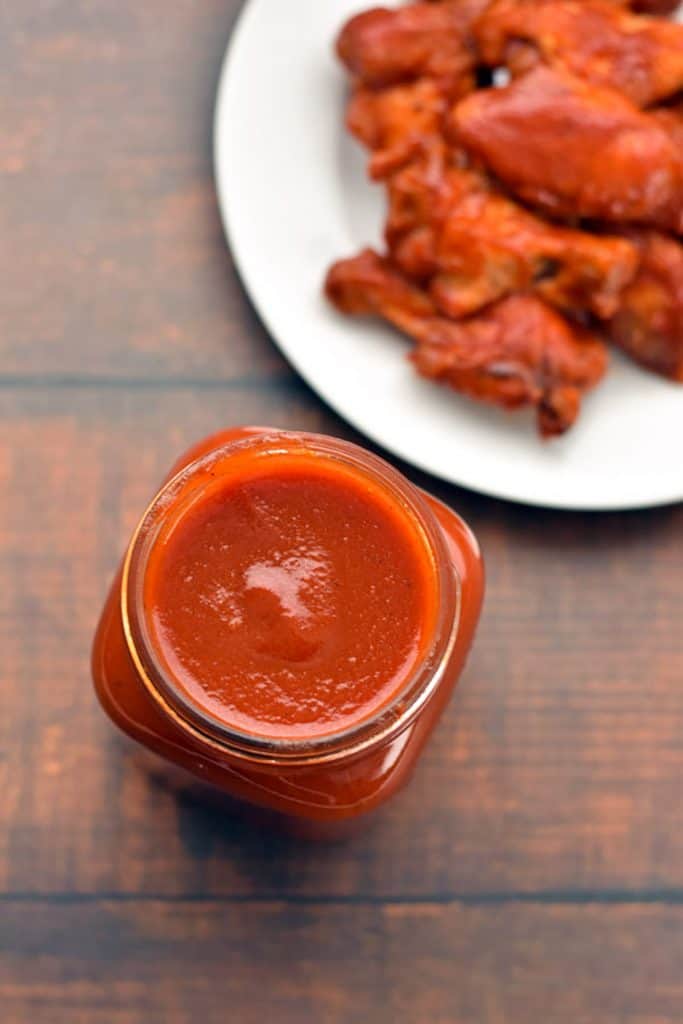 overhead shot of a jar of low fodmap bbq sauce next to a plate of BBQ chicken wings