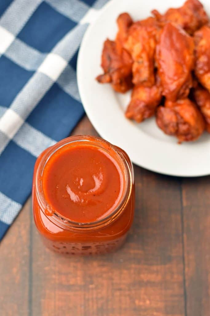 overhead shot of a jar of low FODMAP BBQ sauce in front of chicken wings and a blue and white checkered towel