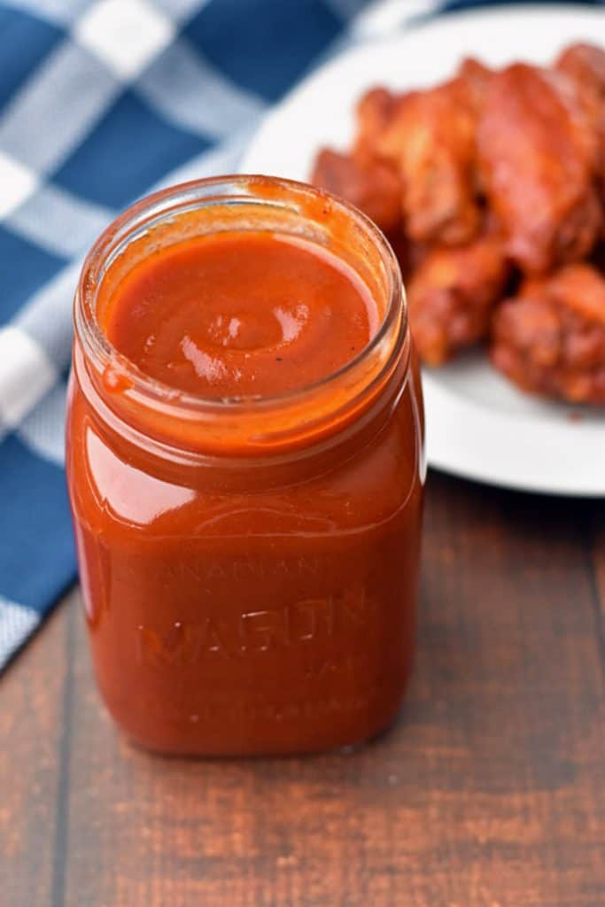 low fodmap BBQ sauce in a jar front of a plate of chicken wings and a blue and white checkered towel