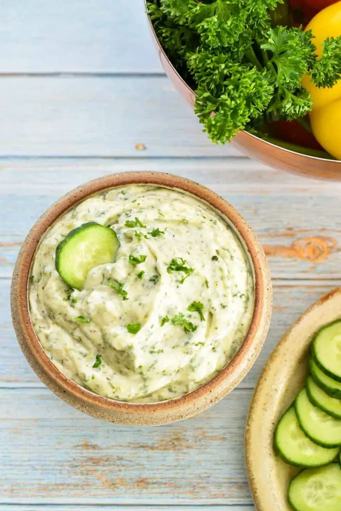 a bowl of low fodmap veggie dip (dairy-free, Paleo, Whole30) with a slice of dipped cucumber next to a plate of sliced cucumbers and a bowl of vegetables