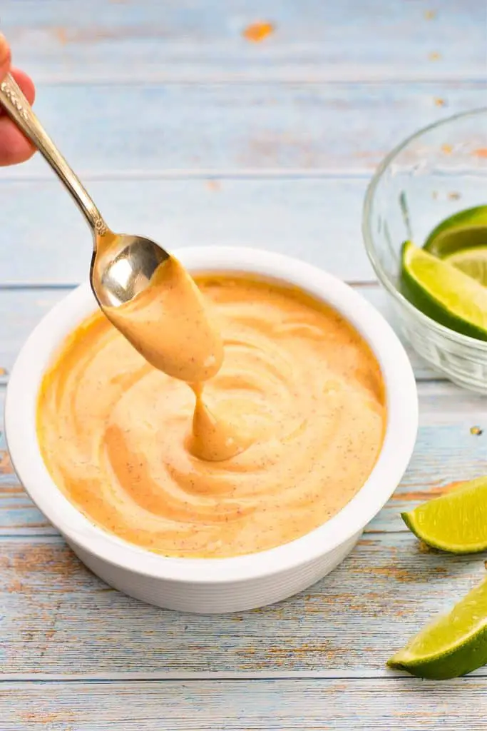 a spoon being dipped into low fodmap chipotle mayo next to a bowl of lime wedges