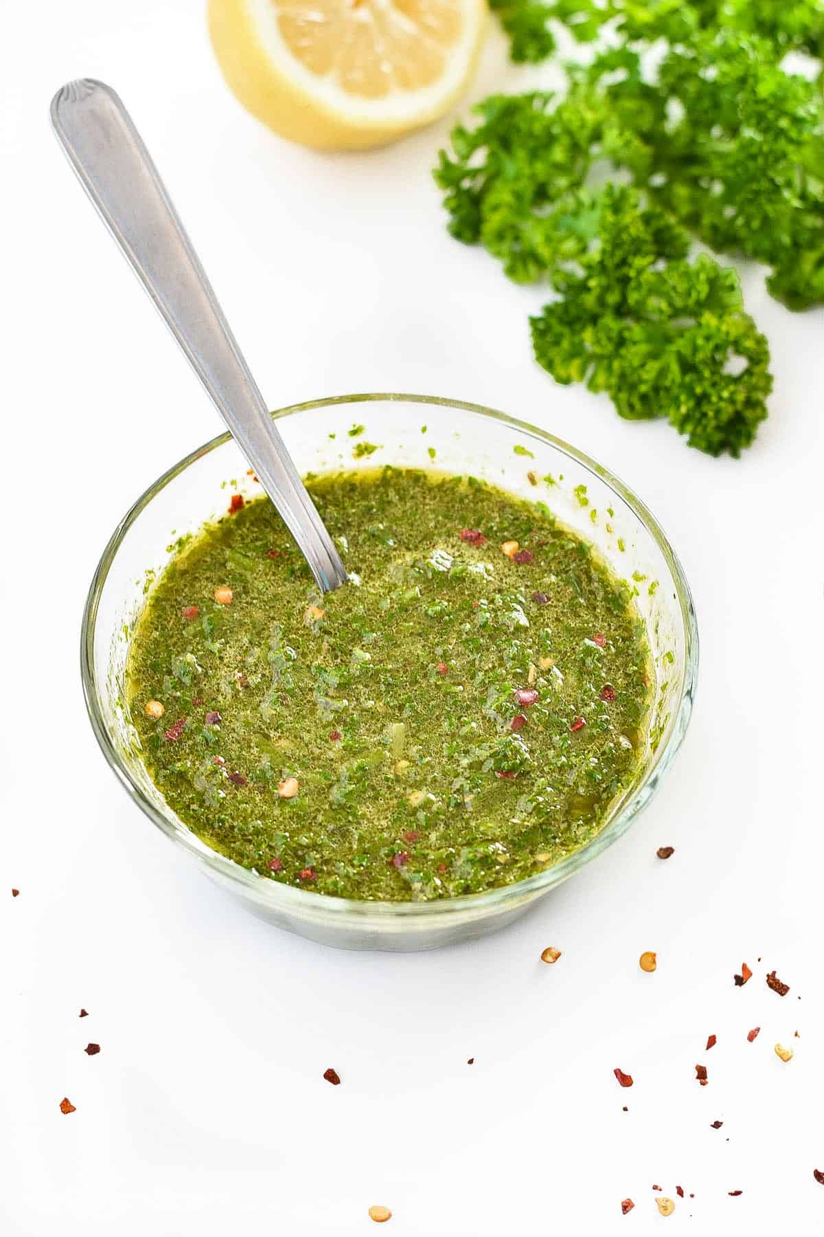 a bowl of low fodmap chimichurri sauce in front of a lemon and parsley