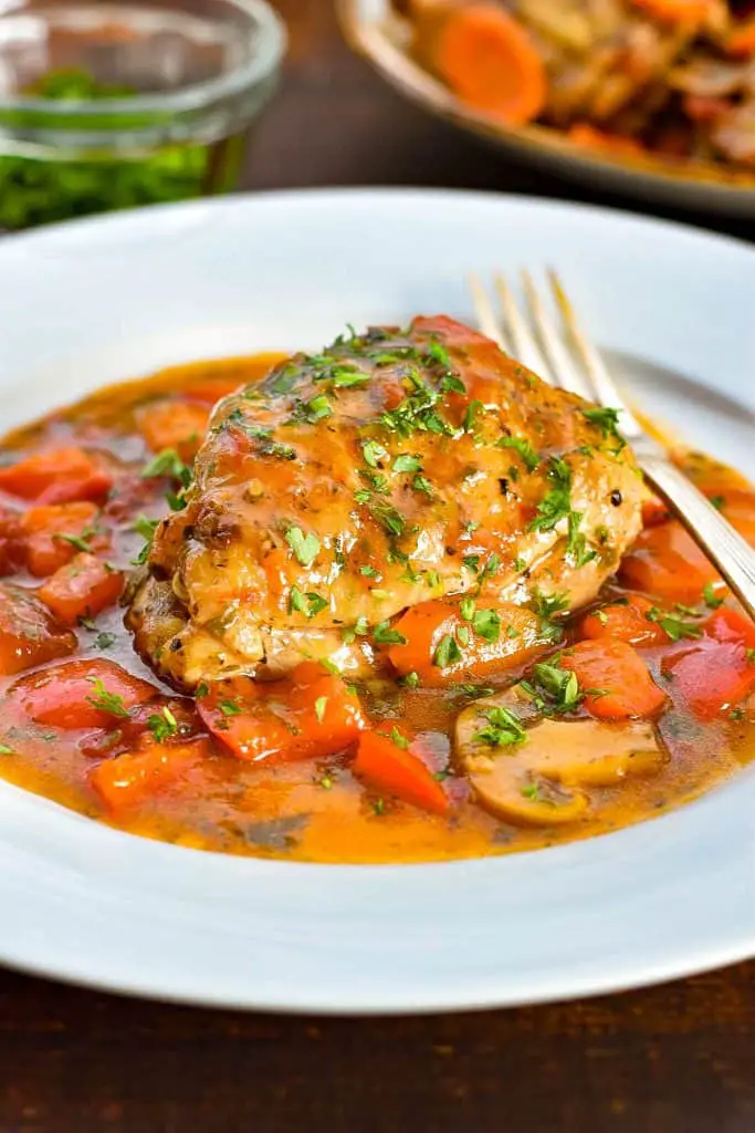 low fodmap chicken cacciatore on a white plate with a fork garnished with chopped parsley