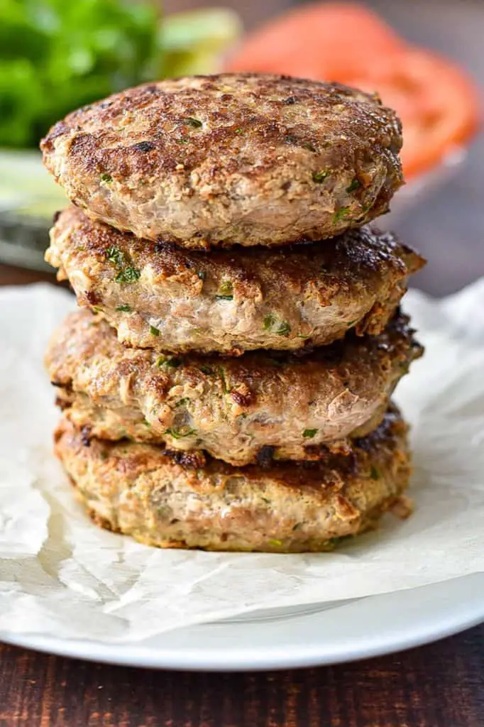 low fodmap turkey burgers in a stack on parchment paper in front of burger toppings
