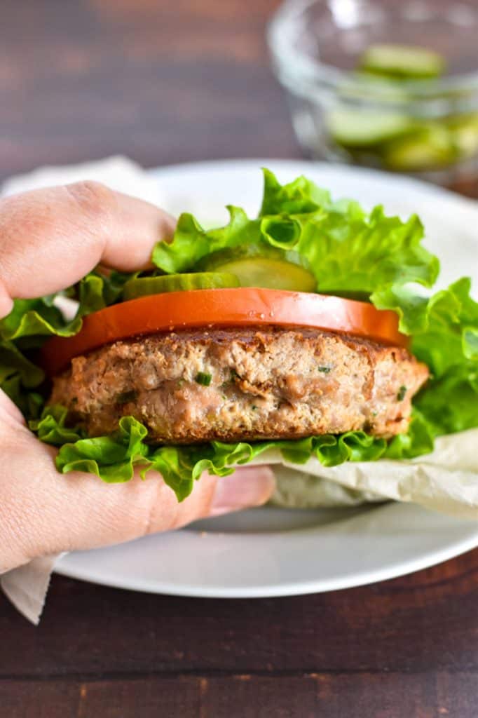 a hand holding a low fodmap whole30 turkey burger in a lettuce bun with tomato and pickle
