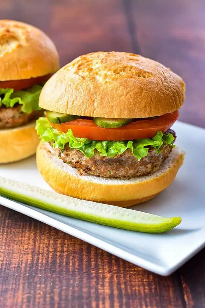 two low fodmap turkey burgers on gluten-free buns on a white plate with a pickle spear