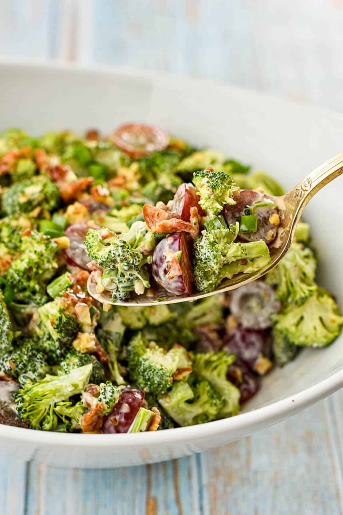 a spoon scooping broccoli salad with bacon out of a white bowl