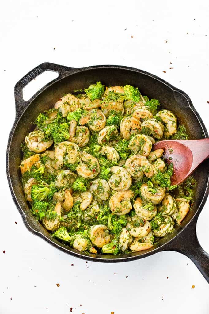 overhead shot of low fodmap chimichurri shrimp and broccoli in a cast iron skillet with a red wooden spoon