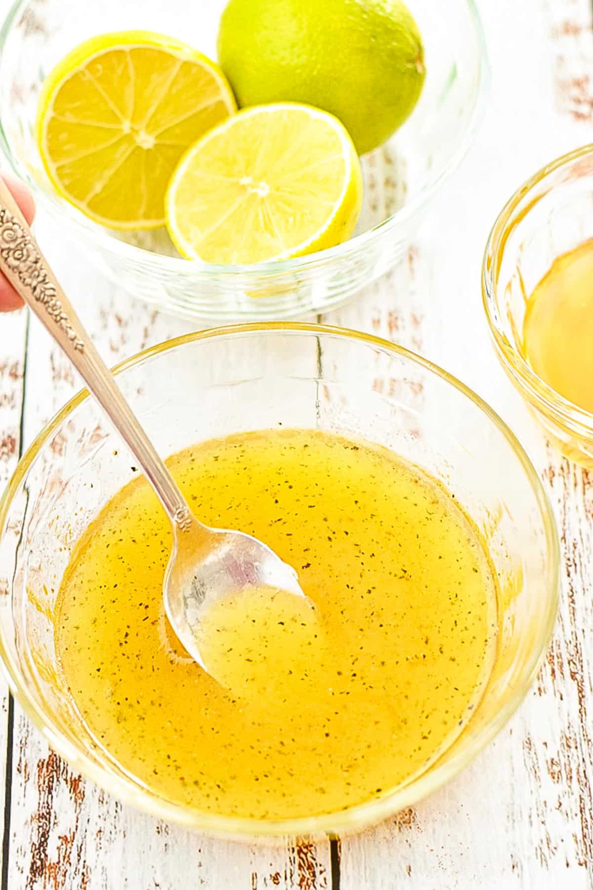 a spoon dipping into a bowl of low fodmap honey lime salad dressing with a bowl of honey and limes behind