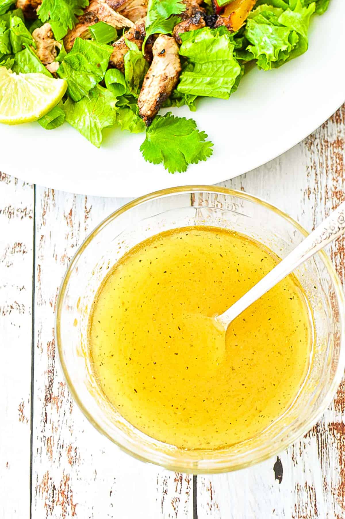 low fodmap honey lime dressing in a glass bowl containing a spoon in front of a salad