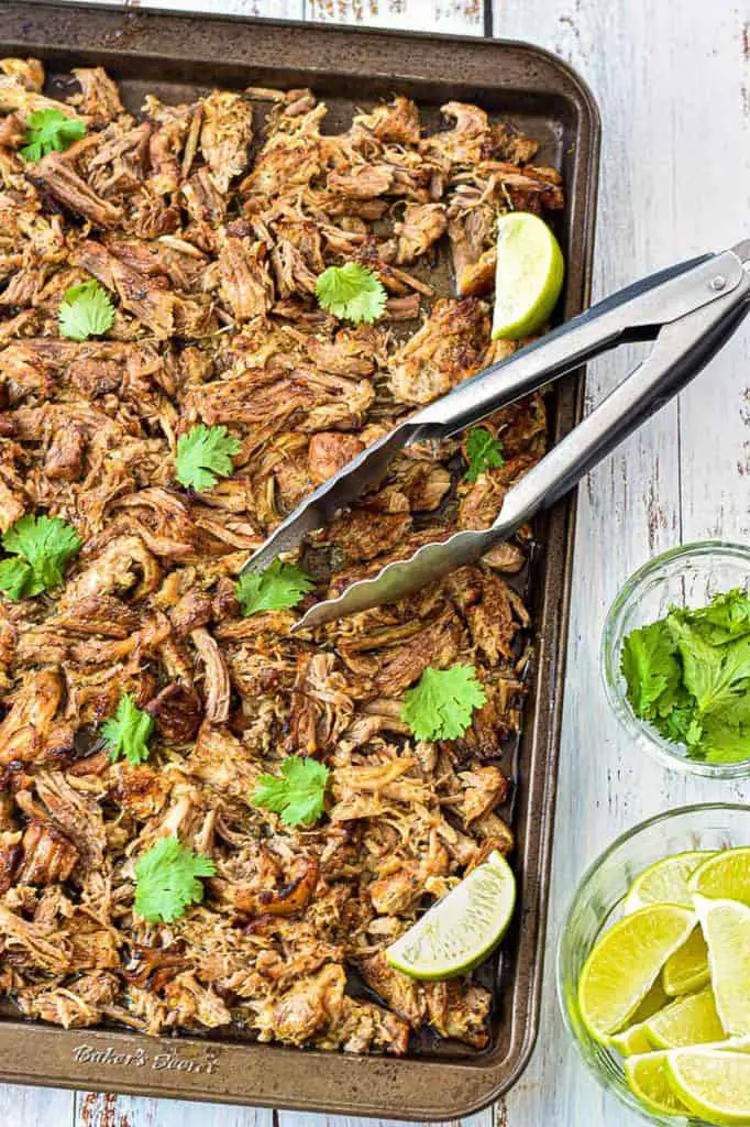 low fodmap instant pot carnitas on a cookie sheet with tongs next to a bowl of limes and cilantro