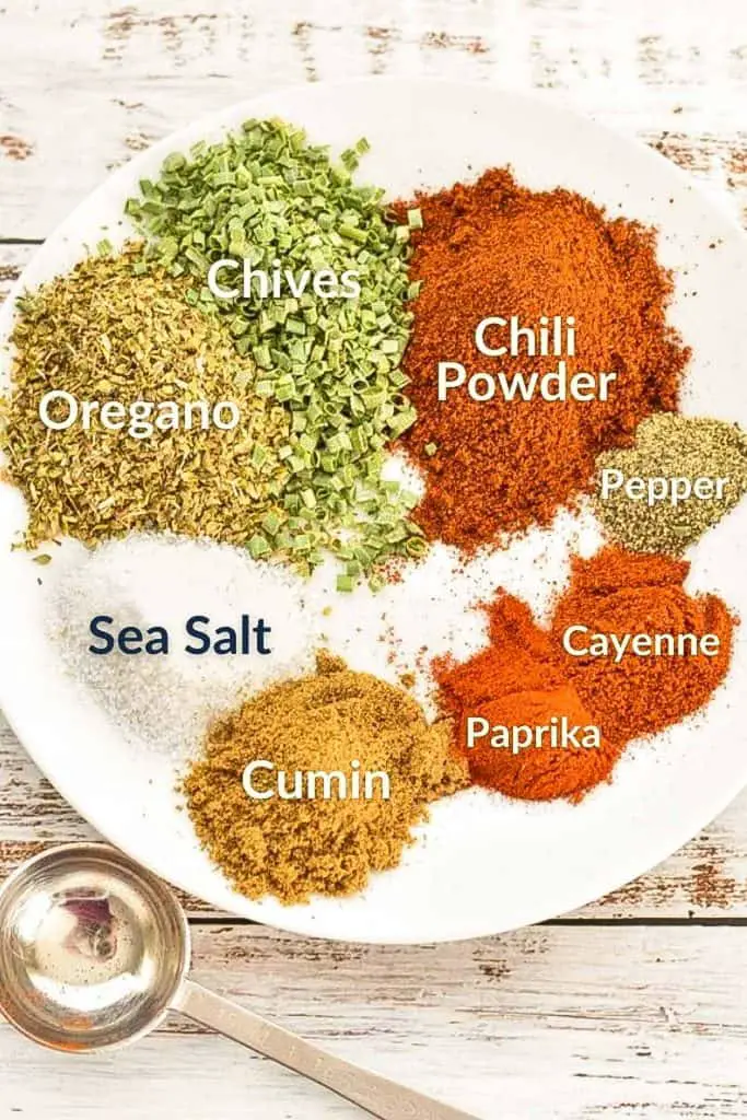 a plate of labeled spices including oregano, chives, chili powder, pepper, cayenne, paprika, cumin and sea salt next to a measuring spoon
