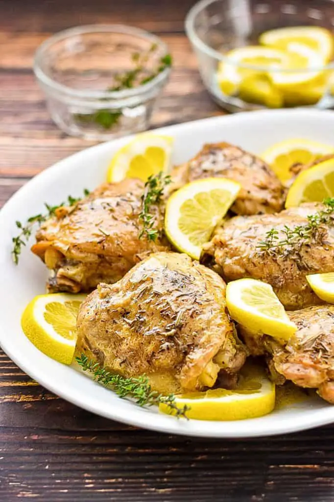 a platter of low fodmap lemon chicken in front of a bowl of lemons and a pitcher of sauce