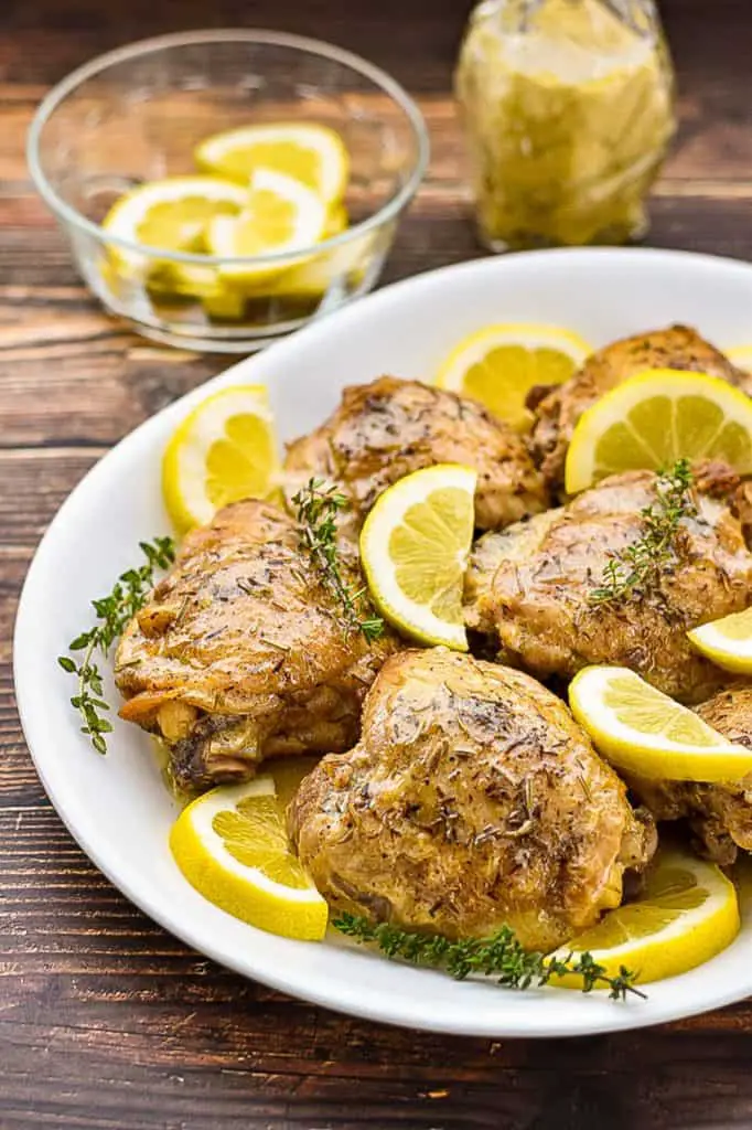 a platter of low fodmap lemon chicken in front of a bowl of thyme sprigs and a bowl of lemon slices