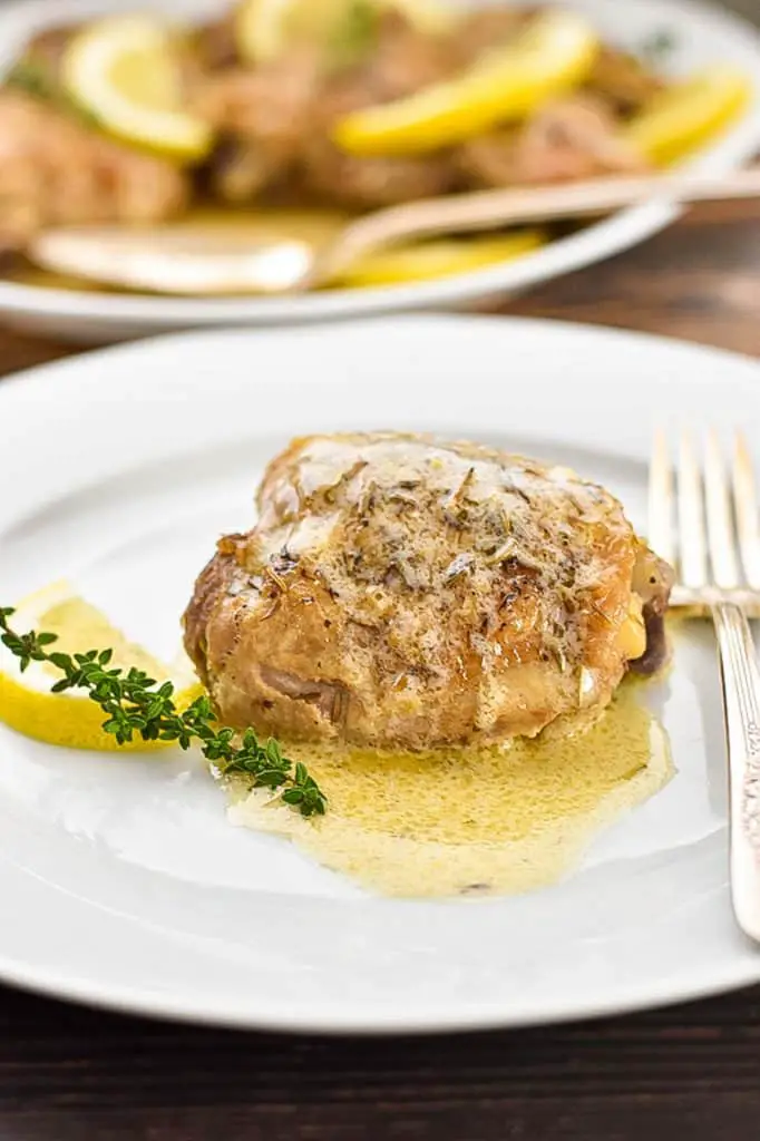 a close up shot of a piece of low fodmap instant pot lemon chicken on a plate with a fork in front of a platter of chicken