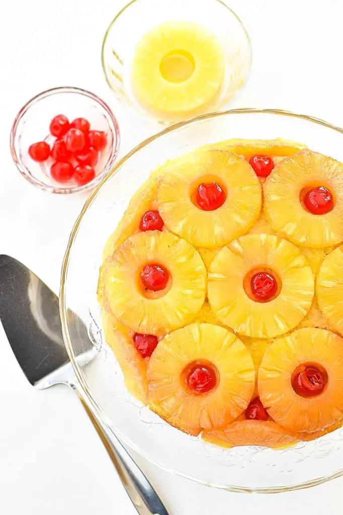 overhead shot of a low fodmap gluten-free pineapple upside down cake with a serving spatula, a bowl of cherries and a bowl of pineapple slices