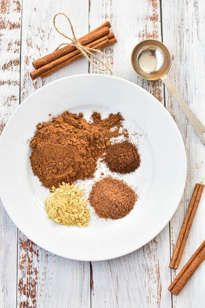 a plate of low FODMAP pumpkin pie spice ingredients next to cinnamon sticks and a tablespoon