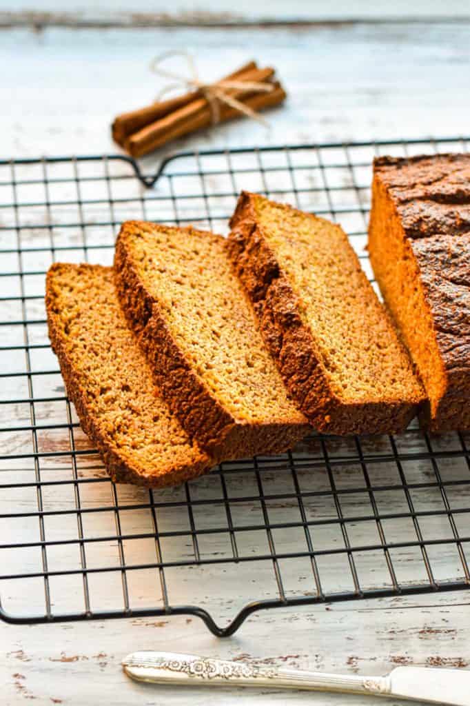 slices of low fodmap pumpkin bread on a wire rack in front of a bunch of cinnamon sticks