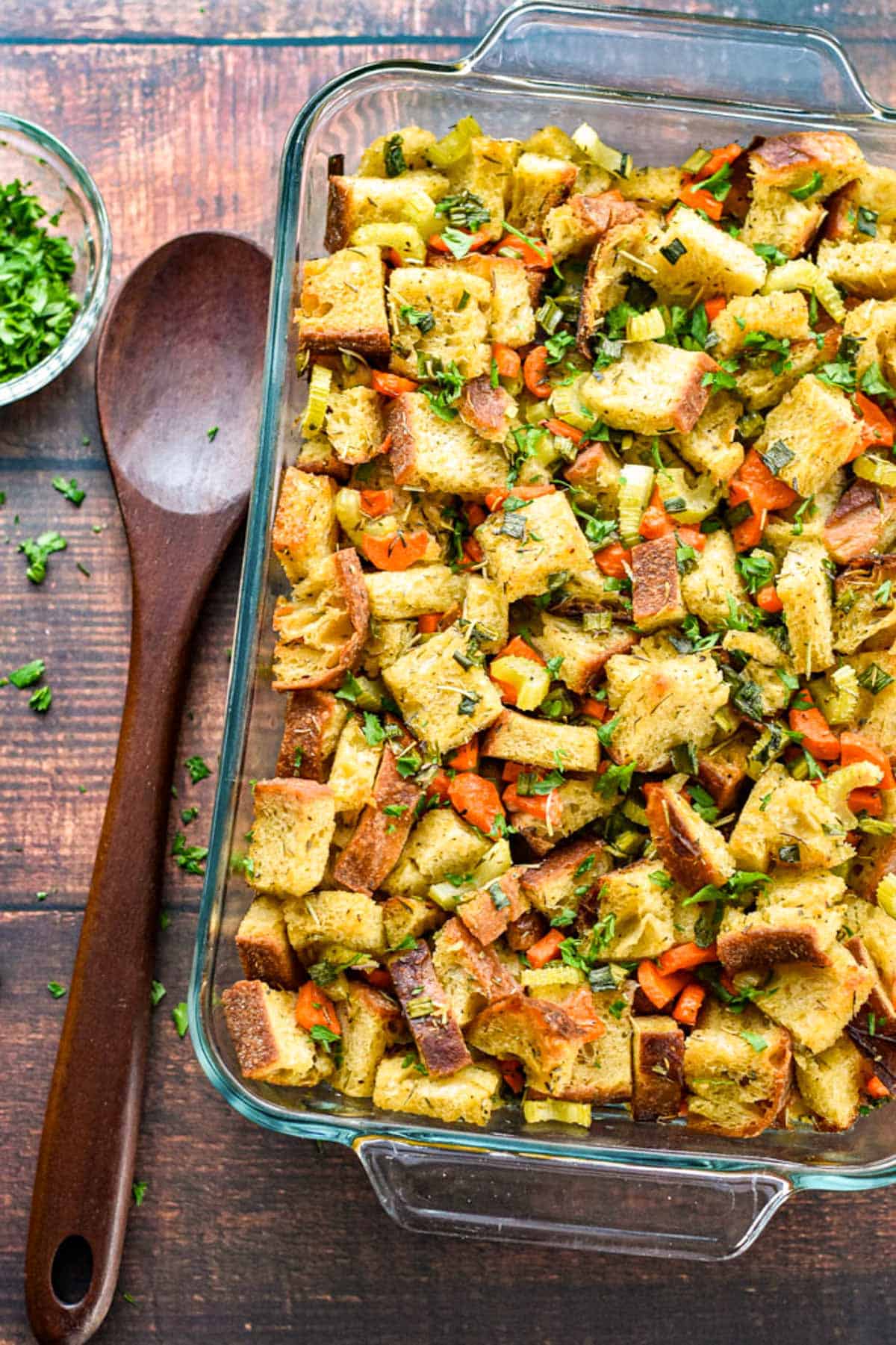 an overhead shot of low fodmap thanksgiving recipe of sourdough stuffing next to a wooden spoon and bowl of chopped parsley