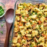 low fodmap sourdough stuffing (dressing) in a glass baking dish next to a wooden spoon and a bowl of chopped parsley.