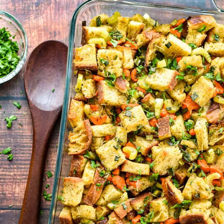 low fodmap sourdough stuffing (dressing) in a glass baking dish next to a wooden spoon and a bowl of chopped parsley.