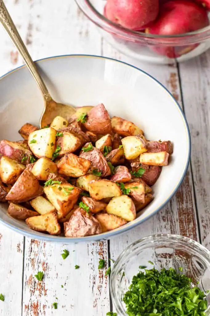 low fodmap air fryer red potatoes in a bowl next to a bowl of whole, red potatoes and a bowl of chopped parsley