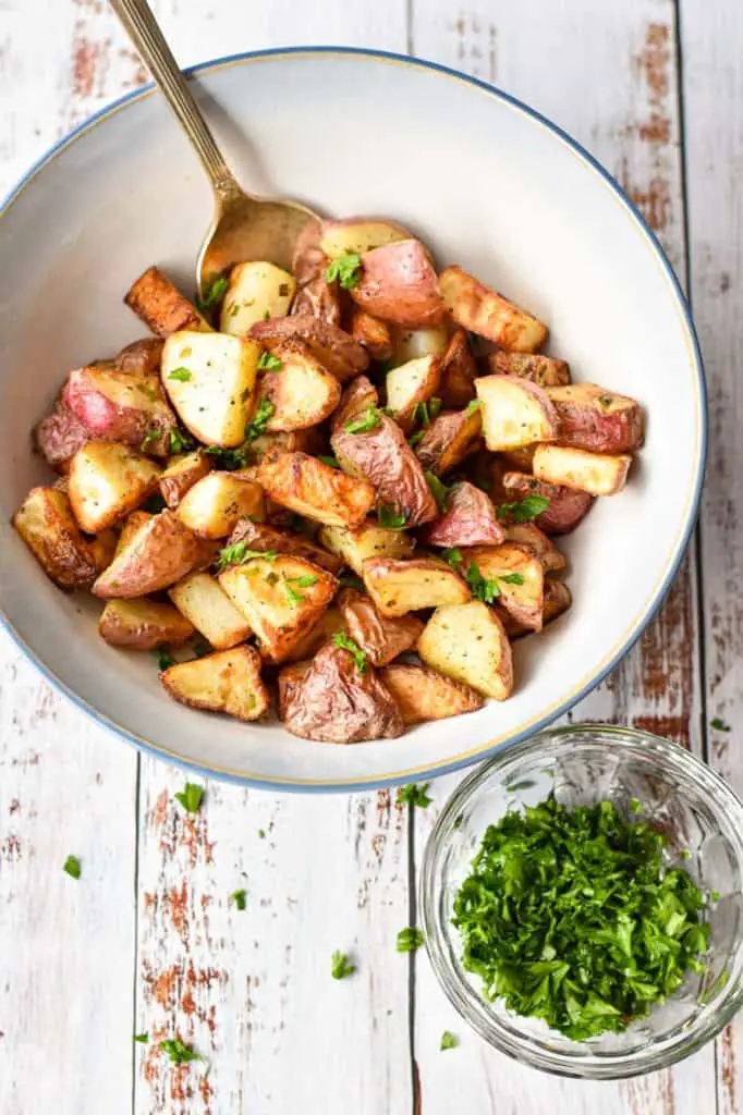 overhead shot of a bowl of low fodmap air fryer red potatoes and a bowl of chopped parsley