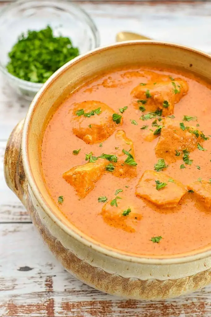 low fodmap butter chicken in a pottery bowl in front of a bowl of chopped parsley