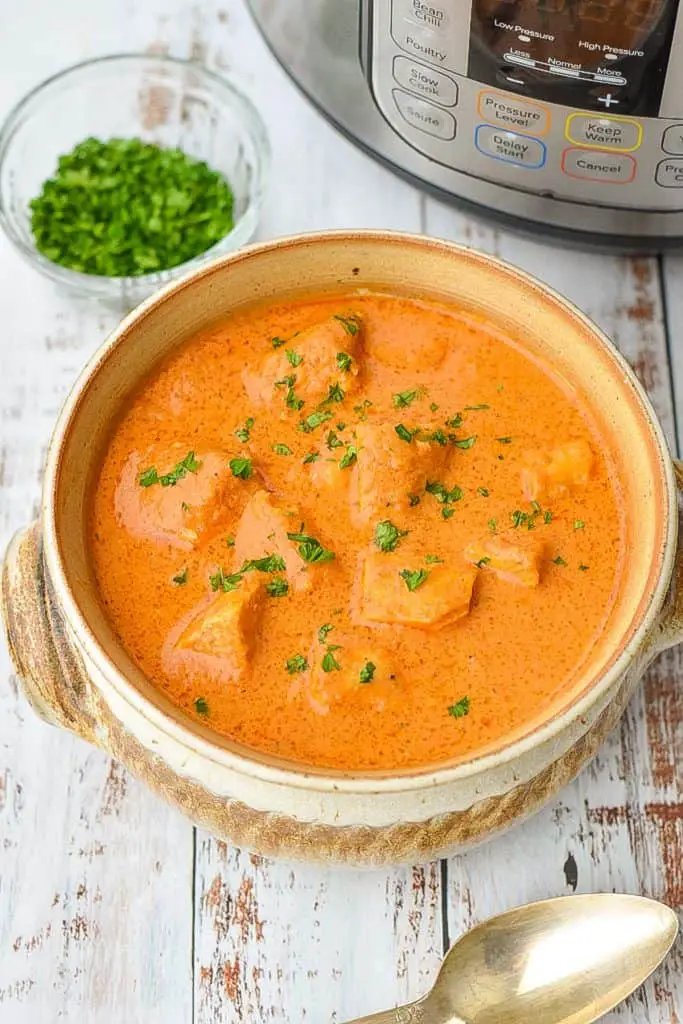 low fodmap butter chicken in a brown pottery bowl in front of an instant pot and a bowl of chopped parsley