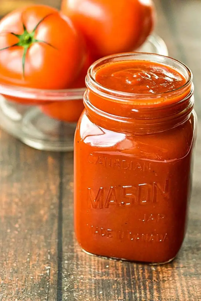 a jar of low fodmap ketchup in front of a bowl of whole tomatoes