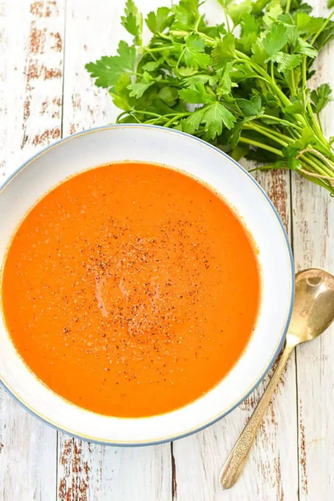 low fodmap tomato soup in a bowl garnished with freshly ground black pepper in front of a bunch of parsley