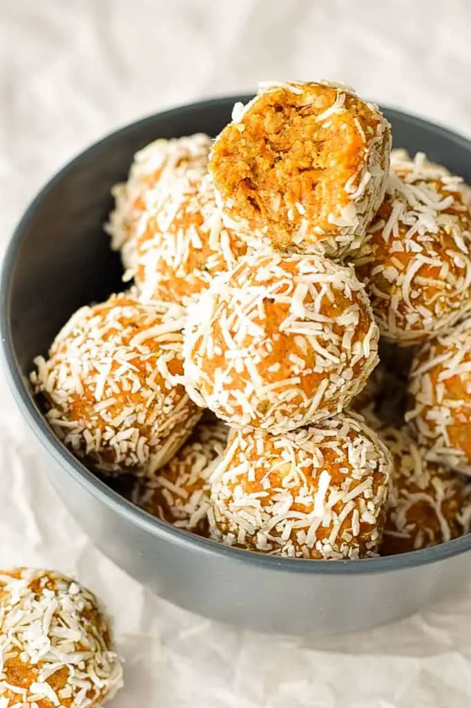 low fodmap carrot cake energy balls in a navy blue bowl with a bite taken out of the top protein ball, showing the interior