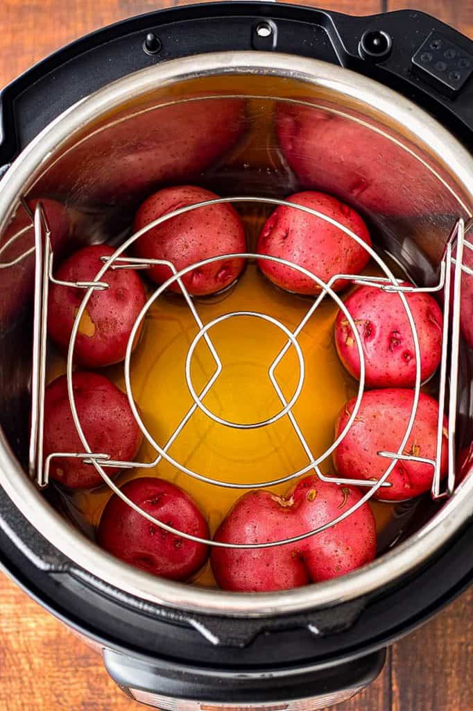 overhead view of the instant pot, with beef broth and red potatoes in the bottom of the inner pot with the trivet resting evenly on top of the potatoes
