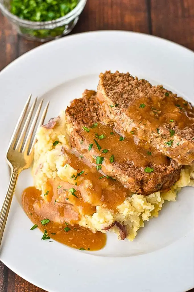 two slices of low fodmap meatloaf resting on top of mashed potatoes topped with gravy on a white plate with a fork