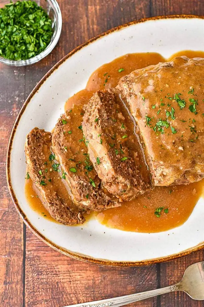 overhead shot of low fodmap instant pot meatloaf on a brown rimmed platter covered in gravy and garnished with parsley
