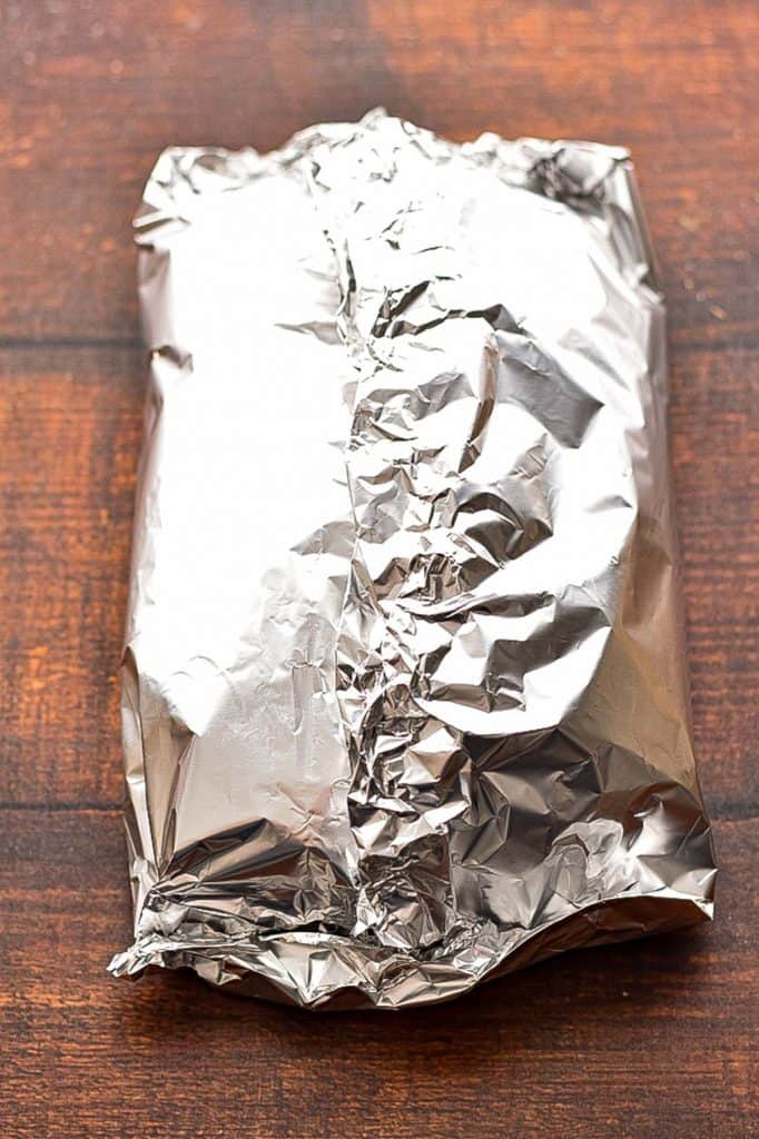 meatloaf wrapped in tinfoil on a brown wood surface