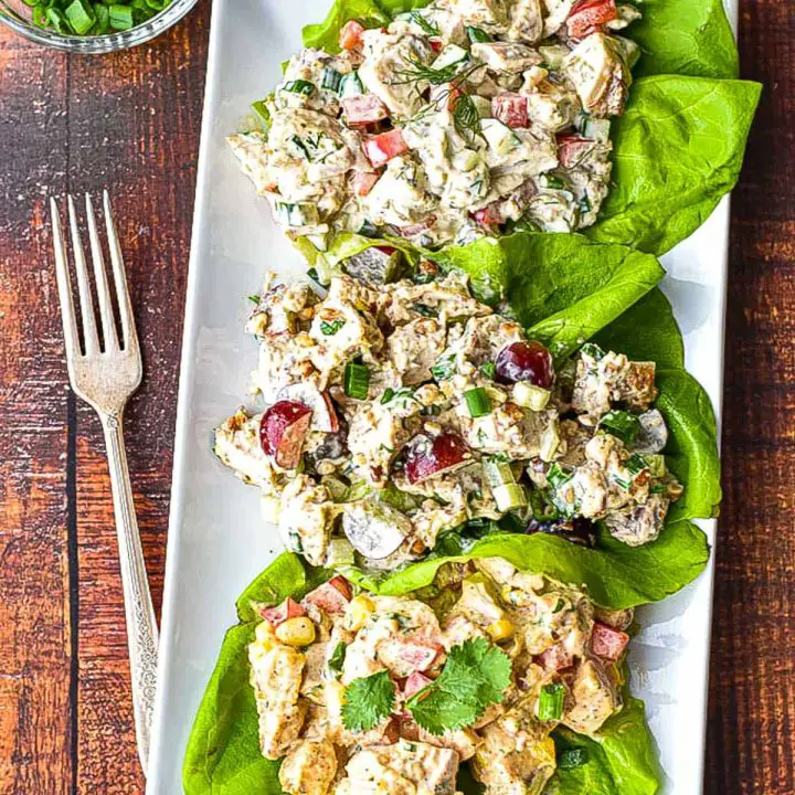three low fodmap chicken salad on butter lettuce on a rectangular white plate next to a fork and a bowl of chopped scallion greens.