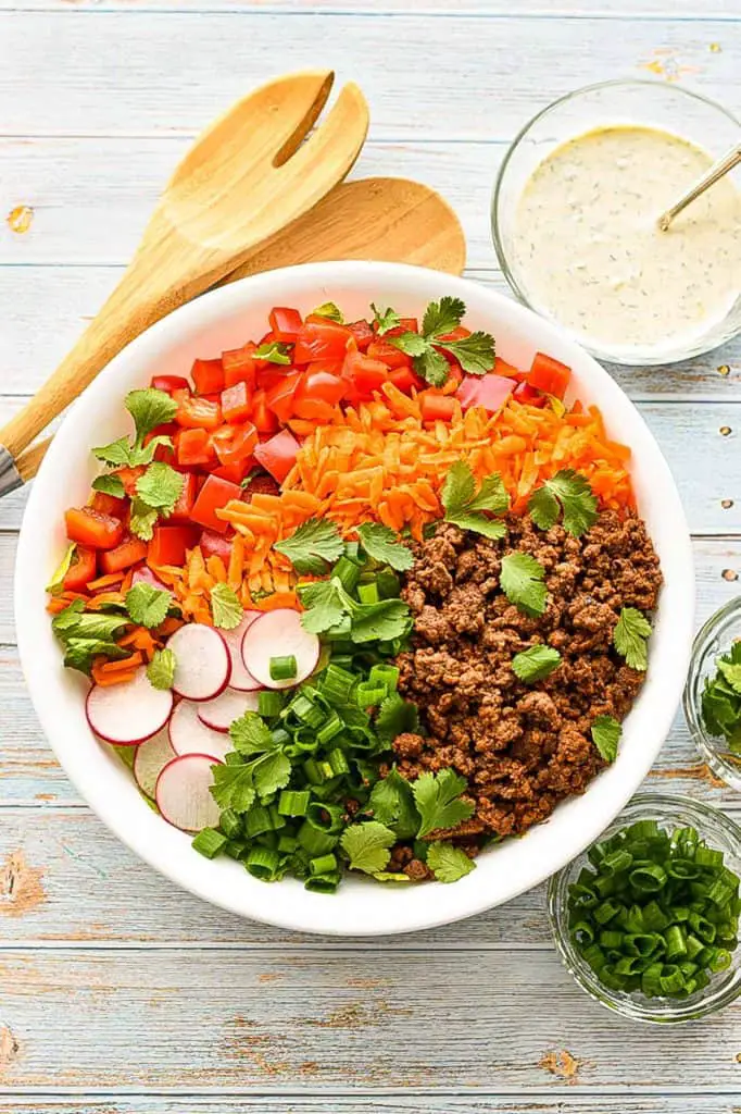 low fodmap taco salad in a white bowl next to bowls of low fodmap ranch dressing, chopped scallions and cilantro leaves