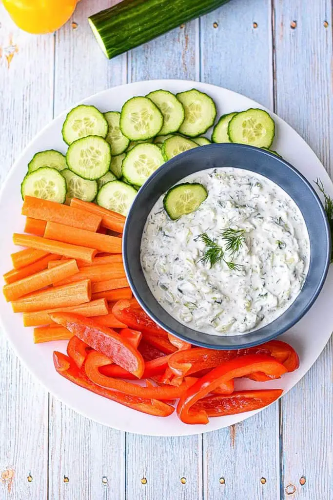 overhead shot of low fodmap tzatziki sauce on a plate with chopped cucumbers, carrots and red bell pepper