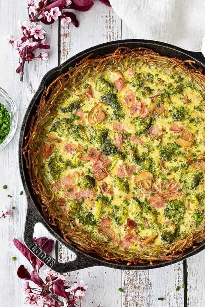 overhead shot of low fodmap quiche with ham, broccoli, and mushrooms and a gluten-free hash brown crust in a cast iron skillet