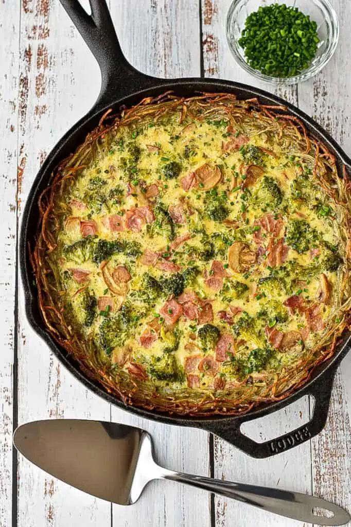 gluten-free quiche in a cast iron skillet next to a pie server on a white background